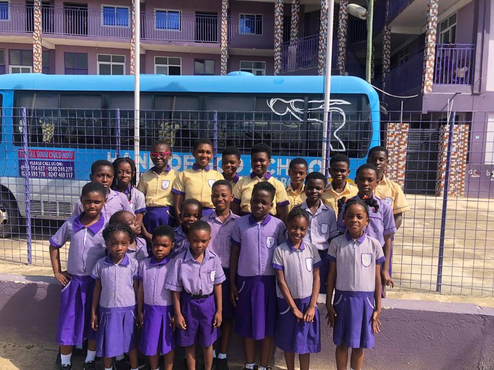 Pupils of Hand of God International School in school uniform, outside the school building with the school bus behind them